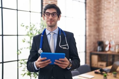 Ofiste doktor steteskobu takan genç İspanyol bir adam gülümsüyor ve yan tarafa bakıyor.. 