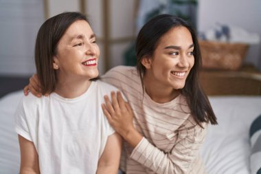 Two women mother and daughter hugging each other sitting on bed at bedroom