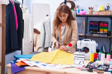 Orta yaşlı kadın elbise fabrikasında kumaş kesiyor.