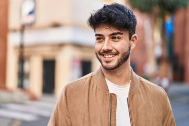 Young hispanic man smiling confident looking to the side at street