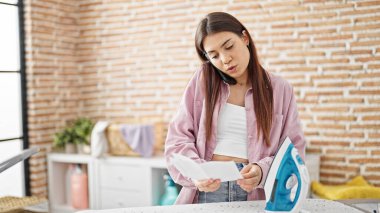 Güzel İspanyol bir kadın akıllı telefondan konuşuyor. Çamaşır odasında ütü makinesi talimatları okuyor.