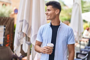 Genç İspanyol adam gülerek sokakta kahve içiyor.