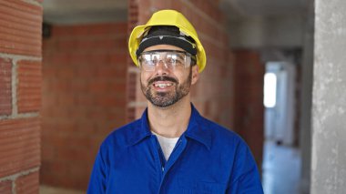 İnşaat alanında gülümseyen kasklı genç İspanyol işçi.