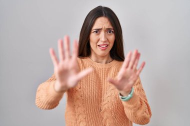 Beyaz arka planda duran genç esmer kadın korku ifadesinden korkuyor ve dehşete düşmüş. El hareketlerini durdur, şok içinde bağır. panik konsepti. 