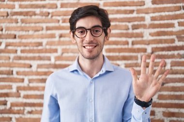 Tuğla duvar arkasında duran İspanyol genç adam beş numarayı gösterip işaret ederken kendinden emin ve mutlu gülümsüyor.. 