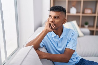 Young latin man looking to the window sitting on sofa at home