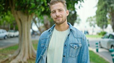 Parkta yüzü ciddi bir ifadeyle duran beyaz bir genç.