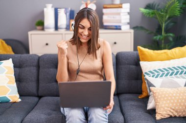 Operatör kulaklığı takarak evden çalışan genç İspanyol kadın gururla bağırıyor, zaferi kutluyor ve başarıyı kollarını kaldırarak heyecanlanıyor. 