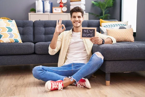 Elinde yeni ev yazısıyla tahtası olan genç İspanyol bir adam parmaklarıyla imza atıyor, gülümseyerek mükemmel bir sembol oluşturuyor. 