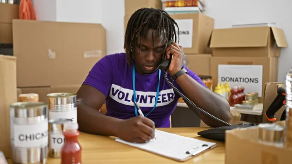 African american man volunteer talking on telephone writing on clipboard at charity center