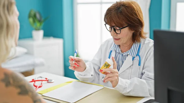 Middle age woman doctor and patient prescribing pills writing on document at clinic