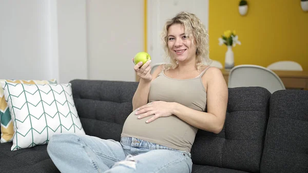 Молодая Беременная Женщина Ест Яблоко Касаясь Живота Дома — стоковое фото