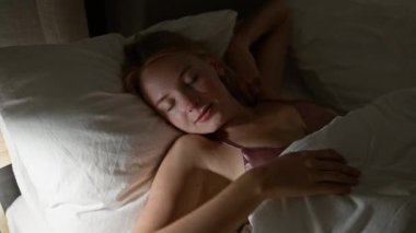 Genç sarışın kadın yatakta uzanıyor, yatak odasında uyuyor.