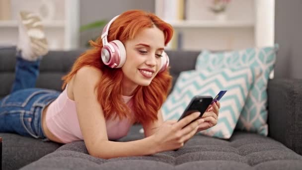 Mladý Ryšavý Žena Nakupování Smartphone Kreditní Karty Poslech Hudby Doma — Stock video
