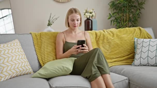 若い金髪の女性が自宅で意見の相違のためにスマートフォンを投げる — ストック動画