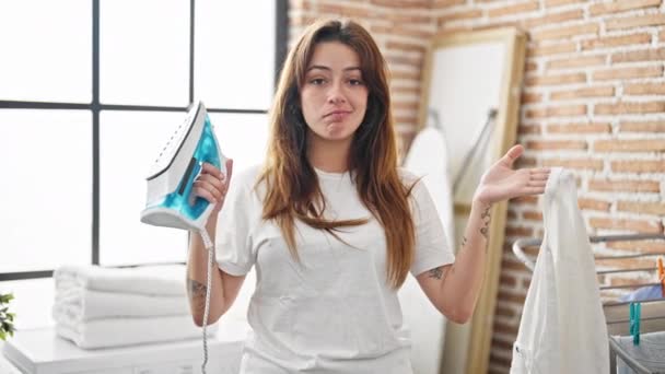 年轻美丽的惊慌失措的女人拿着熨烫机和衬衫 在洗衣房说不 — 图库视频影像