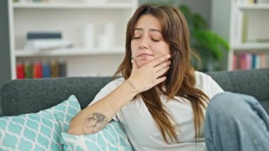 Young beautiful hispanic woman sitting on sofa with serious expression at home