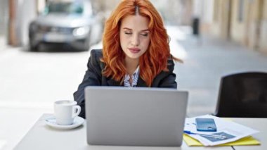 Genç, kızıl saçlı, iş kadını. Laptop kullanıyor. Kahve dükkanının terasında gülümsüyor.