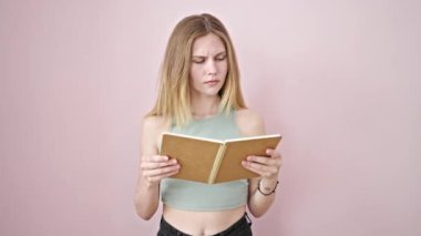 Kitap okuyan genç sarışın kadın pembe arka plandan dolayı üzgün görünüyor.