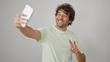 Genç İspanyol adam gülümsüyor. Akıllı telefonun yanında özçekim yapıyor. İzole edilmiş beyaz arka planda.