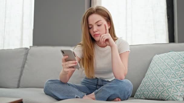 自宅で動揺しているスマートフォンを使用して金髪の若い女性 — ストック動画