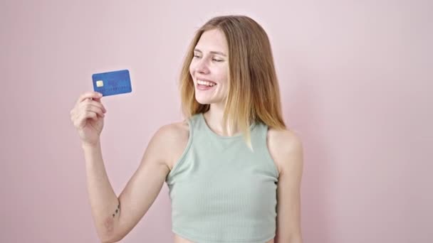 若い金髪の女性は 孤立したピンクの背景の上に勝者のジェスチャーでクレジットカードを持っている自信を持って微笑みます — ストック動画