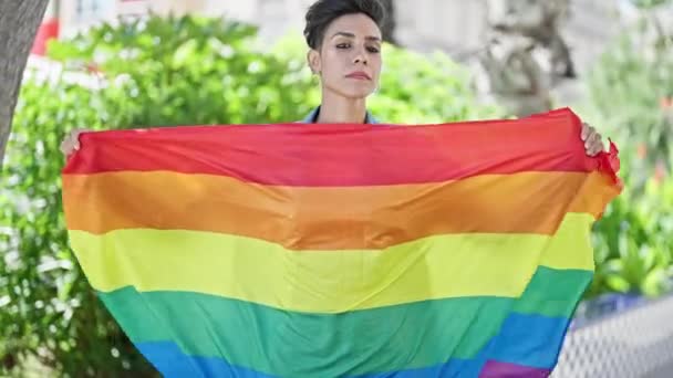 公園で虹の旗を掲げ深刻な表現で立っている若い美しいヒスパニックの女性 — ストック動画