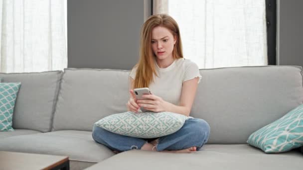 Jovem Loira Jogando Smartphone Sentado Sofá Estressado Casa — Vídeo de Stock