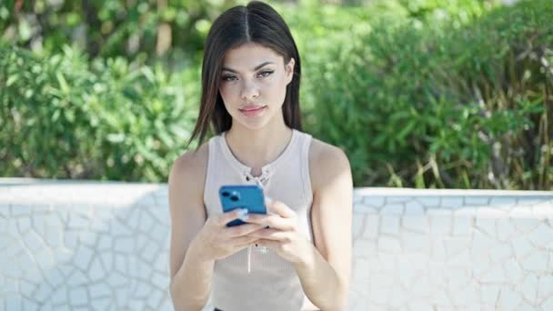 公園でスマートフォンをスマートフォンで笑っている若い白人女性 — ストック動画