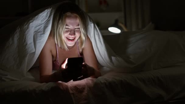 Молодая Блондинка Покрывалом Смартфона Улыбающаяся Спальне — стоковое видео