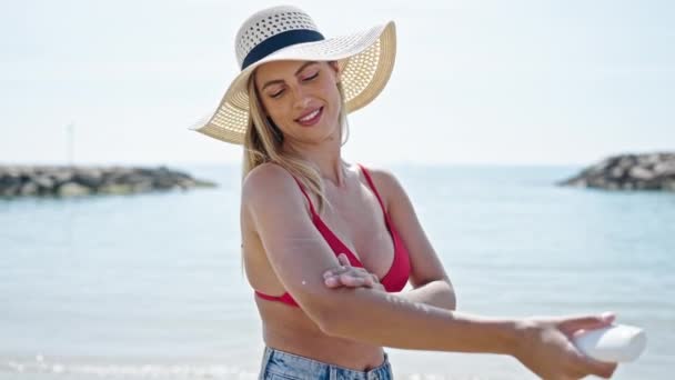 年轻的金发女游客穿着比基尼在海滩涂防晒霜 — 图库视频影像