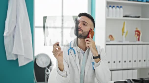 Jovem Hispânico Homem Médico Olhando Xray Falando Smartphone Clínica — Vídeo de Stock