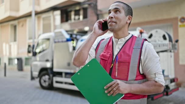 Młody Latynos Wolontariusz Trzymający Notatnik Rozmawiający Przez Telefon Ulicy — Wideo stockowe