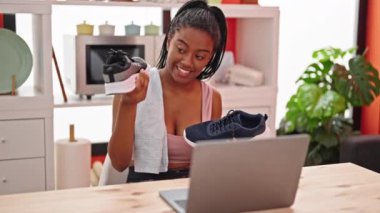 Afro-Amerikalı kadın yemek salonunda spor ayakkabılarını gösteren bir video görüşmesi yapıyor.