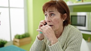 Erişkin İspanyol kadın telefonda konuşuyor ve yemek odasında sigara içiyor.