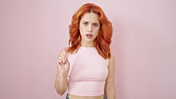 孤立したピンクの背景の上に指のノーと言う深刻な表現で立っている若い赤毛の女性 — ストック動画