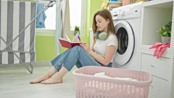 洗濯室で洗濯機を待っているノートを取る若い金髪の女性 — ストック動画