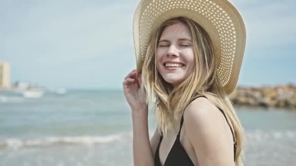 年轻的金发女游客戴着比基尼和夏帽在海滩上微笑 — 图库视频影像