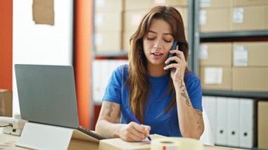 Genç ve güzel İspanyol kadın ecommerce iş işçisi. Ofisteki pakette akıllı telefon yazısıyla konuşuyor.