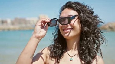Genç ve güzel İspanyol kadın turist, kumsalda kendine güvenen bikini ve güneş gözlüğü takıyor.