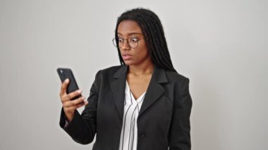 Afrika kökenli Amerikalı iş kadını, beyaz arka planda sürpriz bir ifadeyle akıllı telefona bakıyor.
