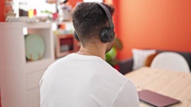 Genç İspanyol adam yemek odasında masada oturmuş müzik dinliyor ve geriye doğru dans ediyor.