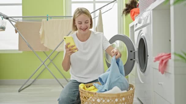 Młoda Blondynka Pomocą Smartfona Pranie Ubrania Uśmiecha Się Pralni — Wideo stockowe
