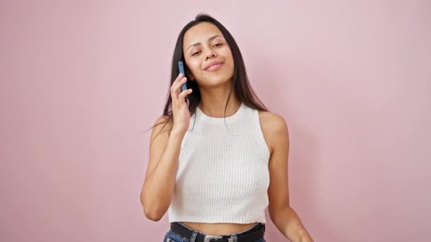 若い美しいヒスパニックの女性は 孤立したピンクの背景の上に提示するスマートフォンで自信を持って話す笑顔 — ストック動画