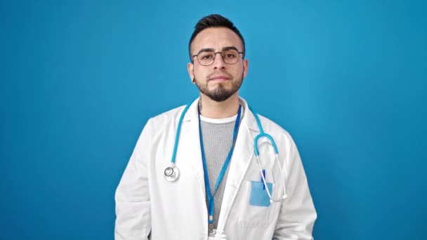 西班牙裔男子医生在孤立的蓝色背景下双手托起胸膛宣誓 — 图库视频影像
