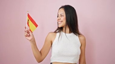 Genç, güzel, İspanyol bir kadın gülümsüyor. İspanyol bayrağını soyutlanmış pembe arka planda tutuyor.