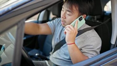 Akıllı telefondan konuşuyor. Sokakta kazanan yüz ifadesiyle arabada oturuyor.