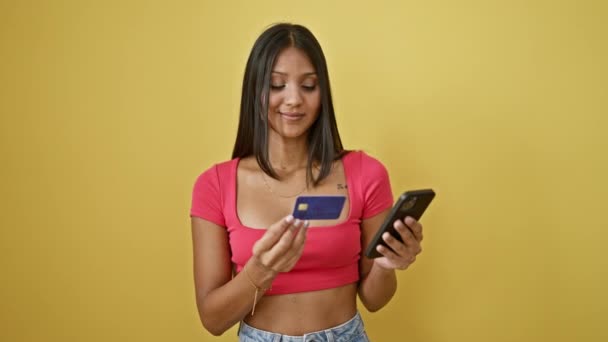単離された黄色の背景上のスマートフォンとクレジットカードで買い物をする若いラテン系女性 — ストック動画