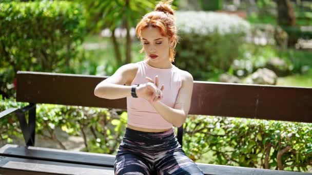 Młoda Ruda Kobieta Odzieży Sportowej Patrząc Zegarek Siedzi Ławce Parku — Wideo stockowe