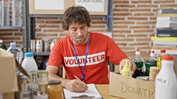 Joven Hispano Voluntario Escribiendo Portapapeles Revisando Productos Centro Caridad — Vídeos de Stock